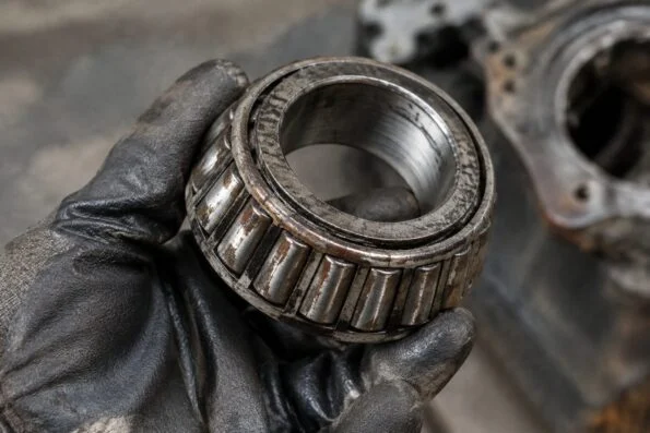 Close-up of a worn tapered roller bearing removed from an old gearbox, held in a gloved hand